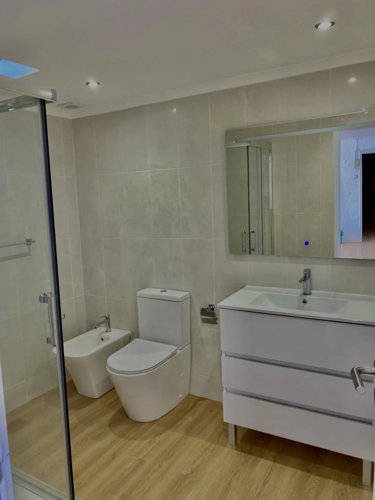 Casa de banho remodelada com móvel branco e pavimento em madeira